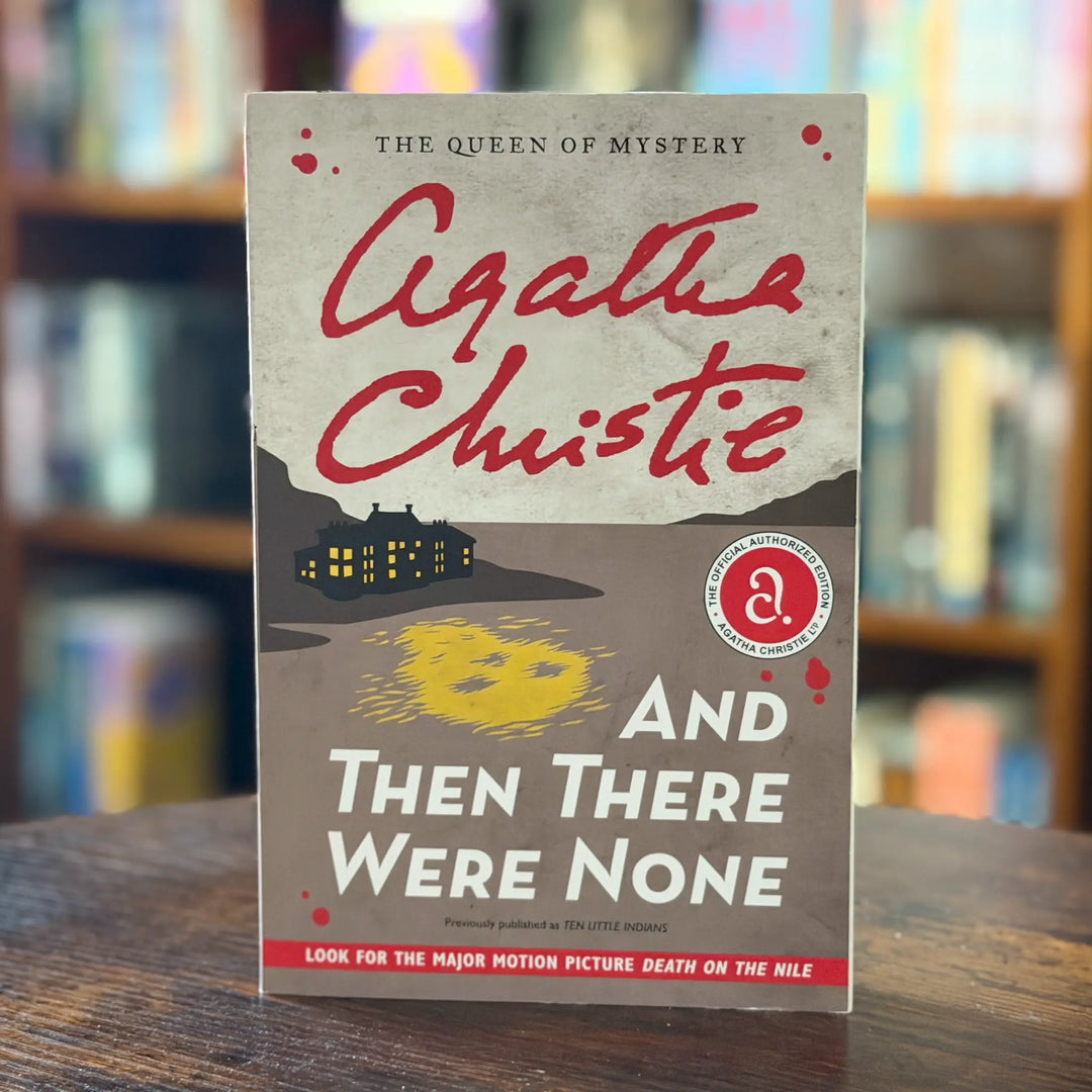 Book cover of 'And Then There Were None' by Agatha Christie on a wooden surface with a blurred bookshelf background.