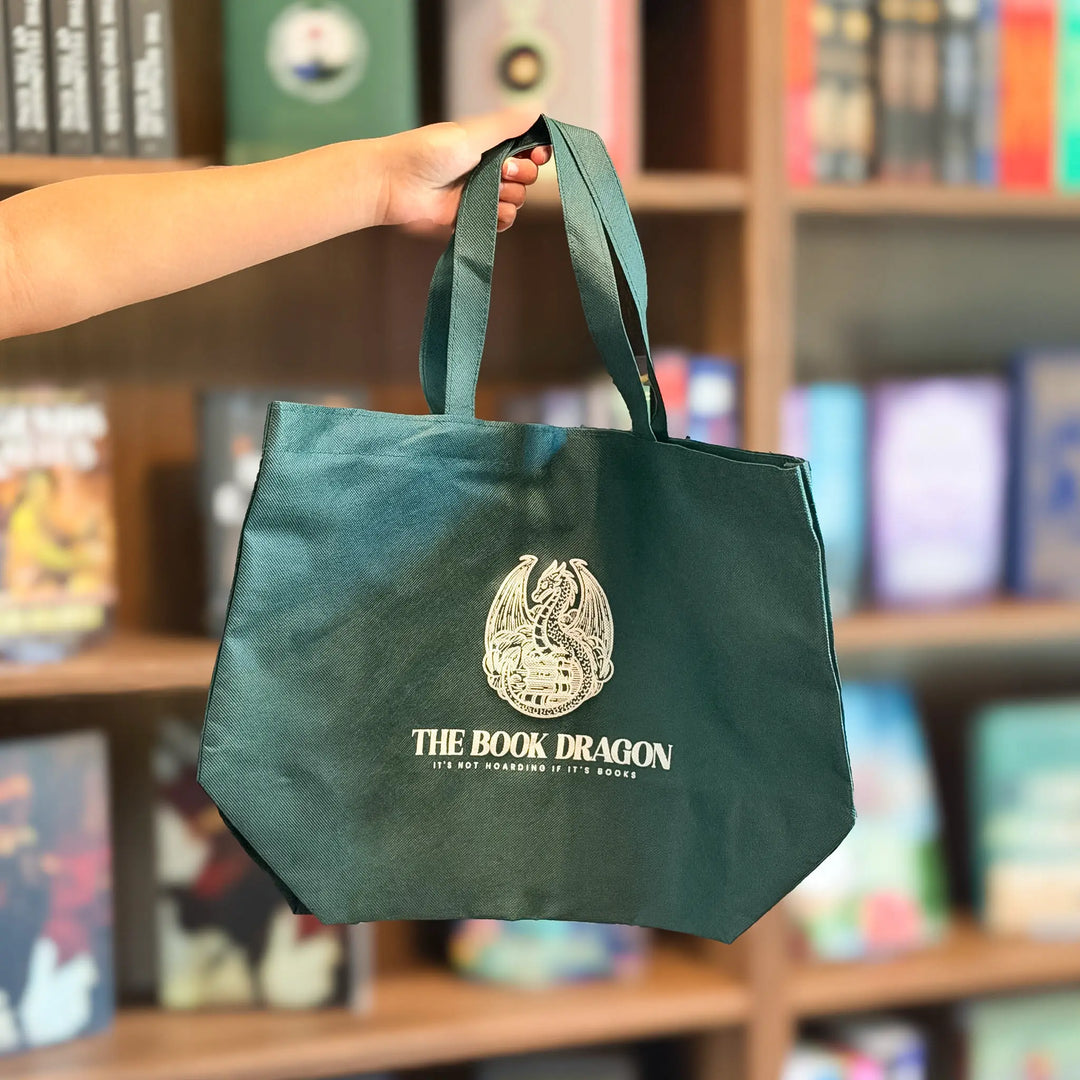 Green tote bag with 'The Book Dragon' logo held in front of a bookshelf.