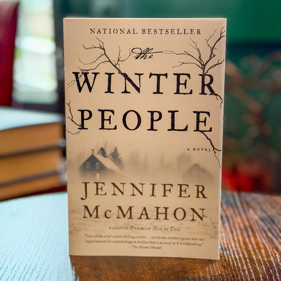 Book titled 'The Winter People' by Jennifer McMahon on a wooden surface with blurred books in the background.
