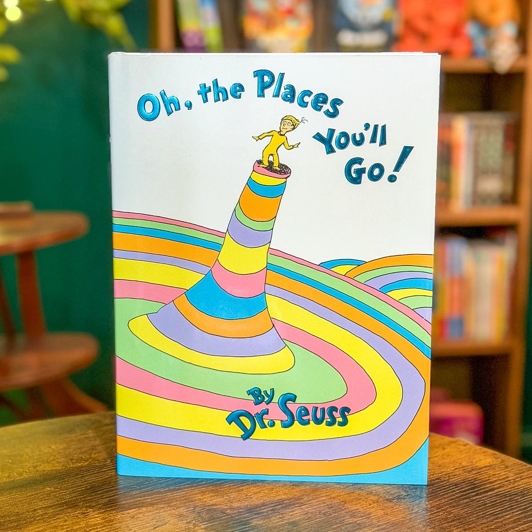 Book titled 'Oh, the Places You'll Go!' by Dr. Seuss on a wooden surface with a blurred bookshelf in the background.