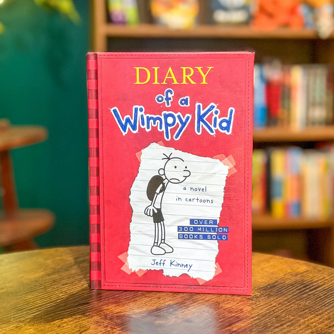 Book titled 'Diary of a Wimpy Kid' on a wooden table with a blurred bookshelf in the background.