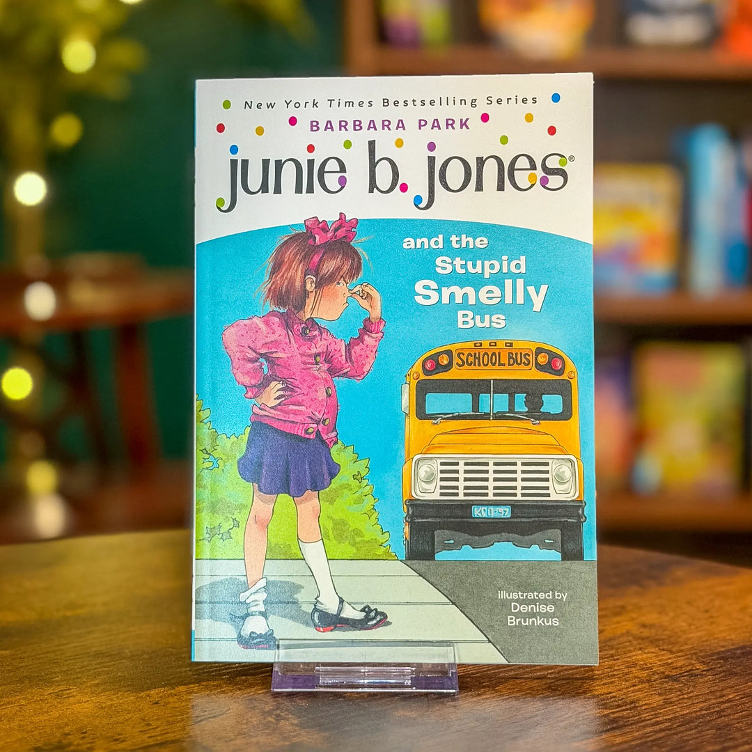 Book titled 'junie b. jones and the Stupid Smelly Bus' by Barbara Park on a wooden surface with a blurred bookshelf background.