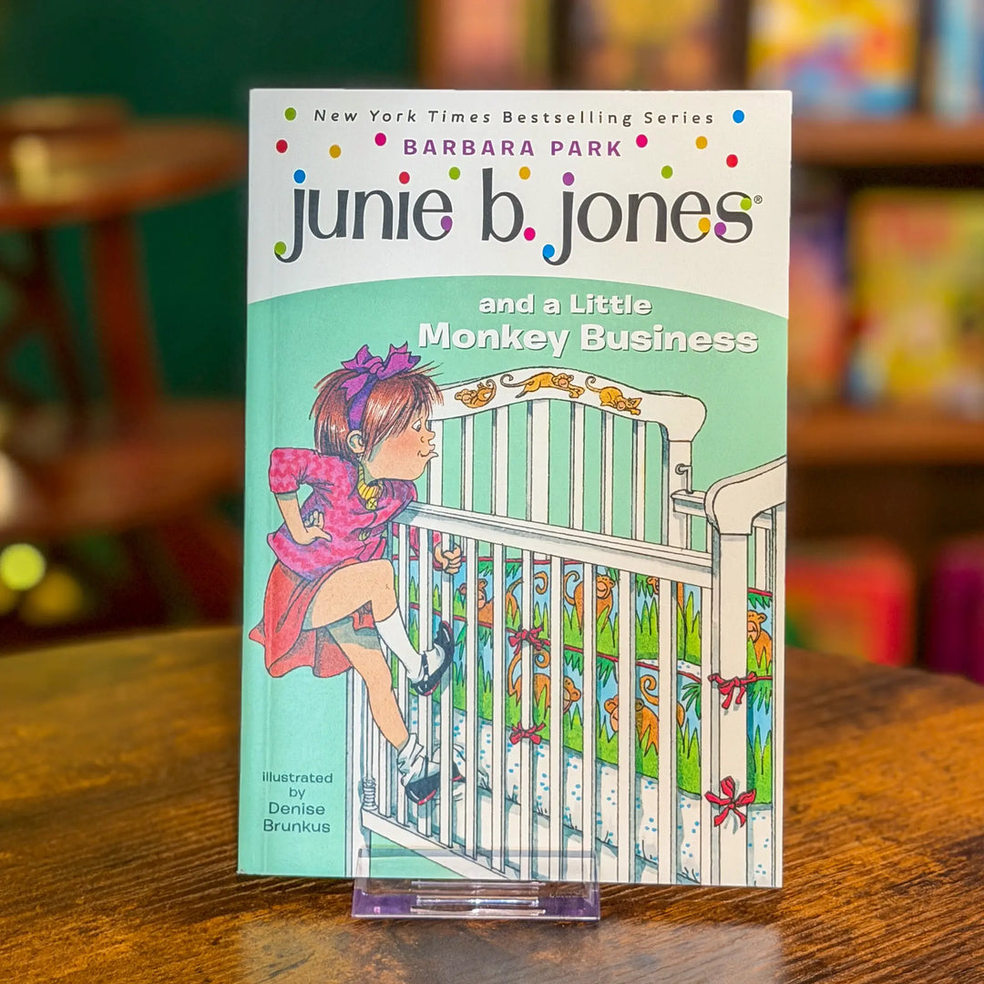 Book titled 'junie b. jones and a Little Monkey Business' by Barbara Park on a wooden surface with a blurred bookshelf background.