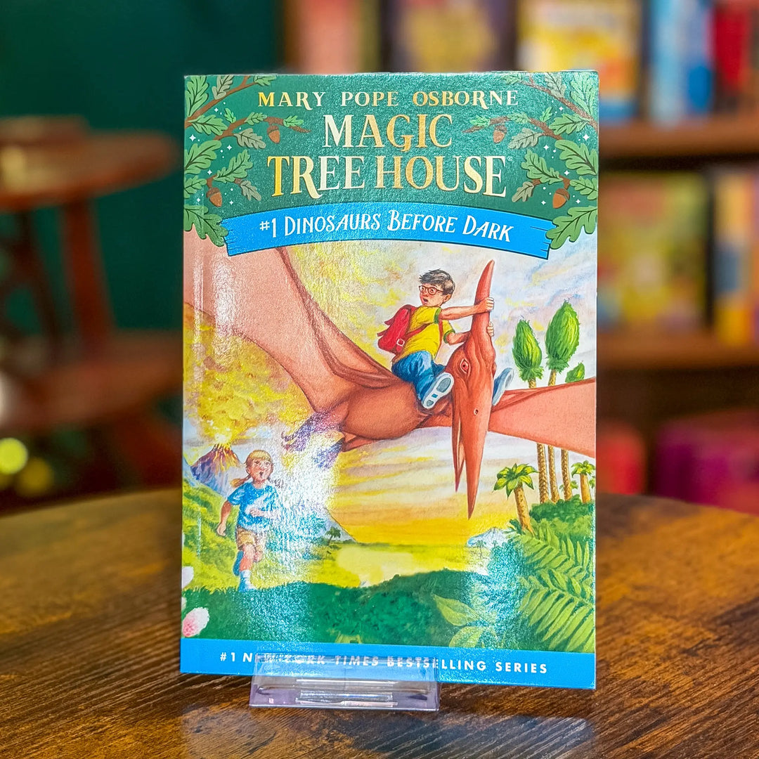 Book titled 'Magic Tree House: Dinosaurs Before Dark' by Mary Pope Osborne on a wooden table.