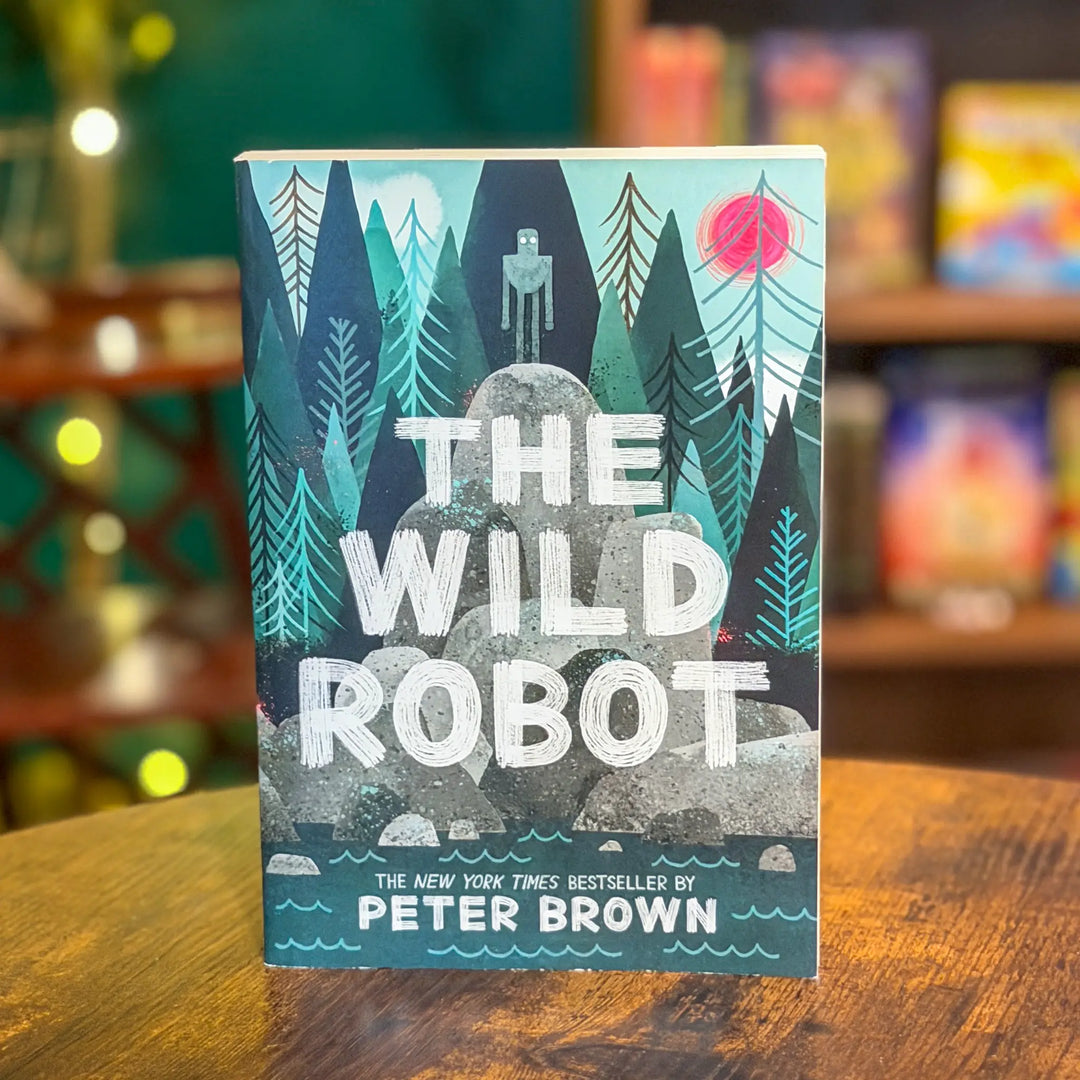 Book cover of 'The Wild Robot' by Peter Brown on a wooden surface with a blurred bookshelf background.