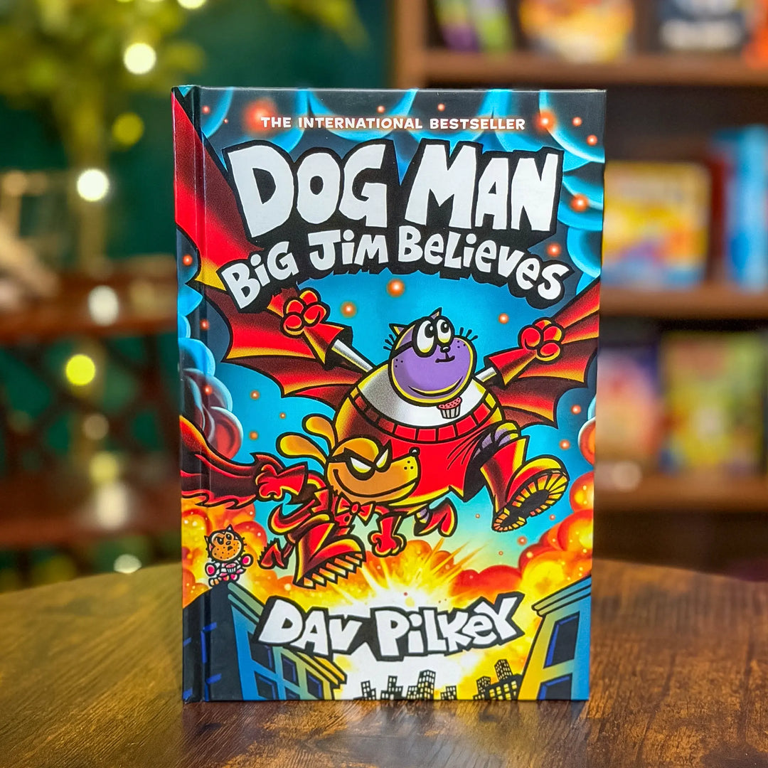 Book titled 'Dog Man Big Jim Believes' by Dav Pilkey on a wooden surface with a blurred bookshelf background.