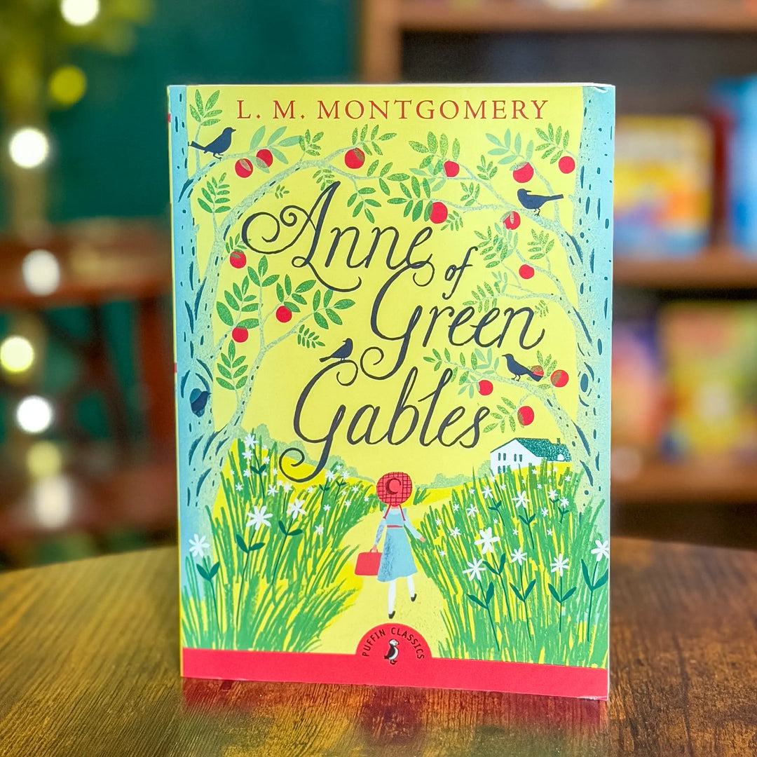 Book titled 'Anne of Green Gables' by L. M. Montgomery on a wooden surface with a blurred bookshelf background.