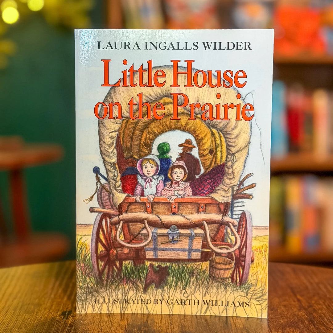 Book cover of 'Little House on the Prairie' with a wagon illustration on a wooden surface.