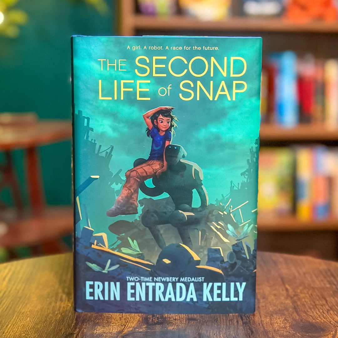 Book titled 'The Second Life of Snap' by Erin Entrada Kelly on a wooden surface with a blurred bookshelf background.