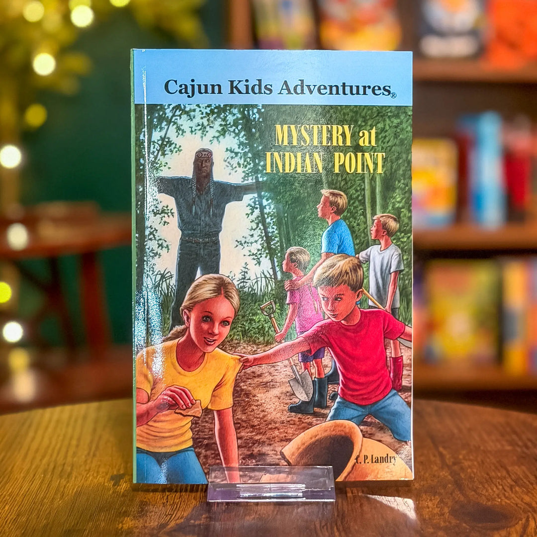 Book titled 'Mystery at Indian Point' from the series 'Cajun Kids Adventures' on a wooden surface with a blurred bookshelf background.