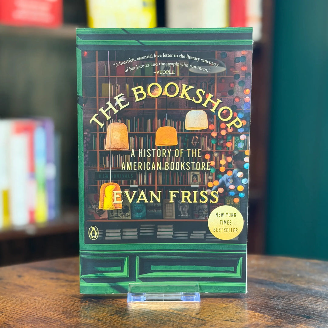 Book titled 'The Bookshop: A History of the American Bookstore' by Evan Fries on a wooden surface with blurred bookshelf in the background.