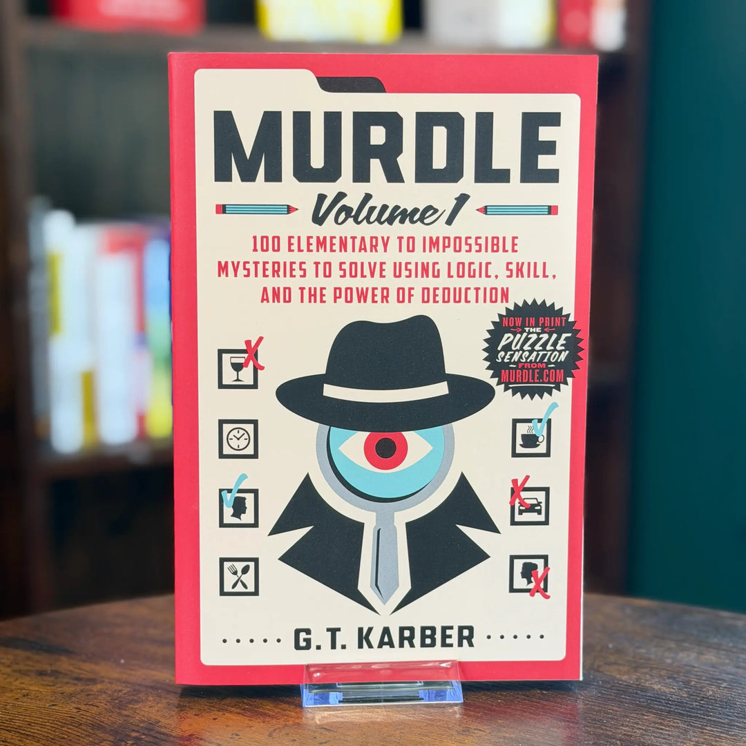 Book titled 'Murdle Volume 1' by G.T. Karber on a wooden surface with a blurred bookshelf background.