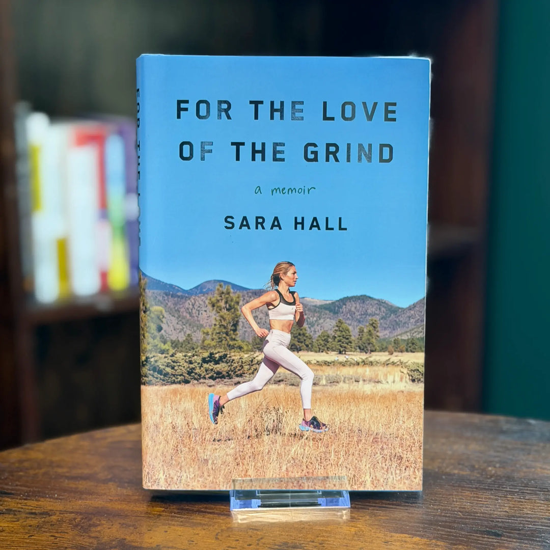 Book titled 'For the Love of the Grind' by Sara Hall with a runner on the cover, placed on a wooden surface.