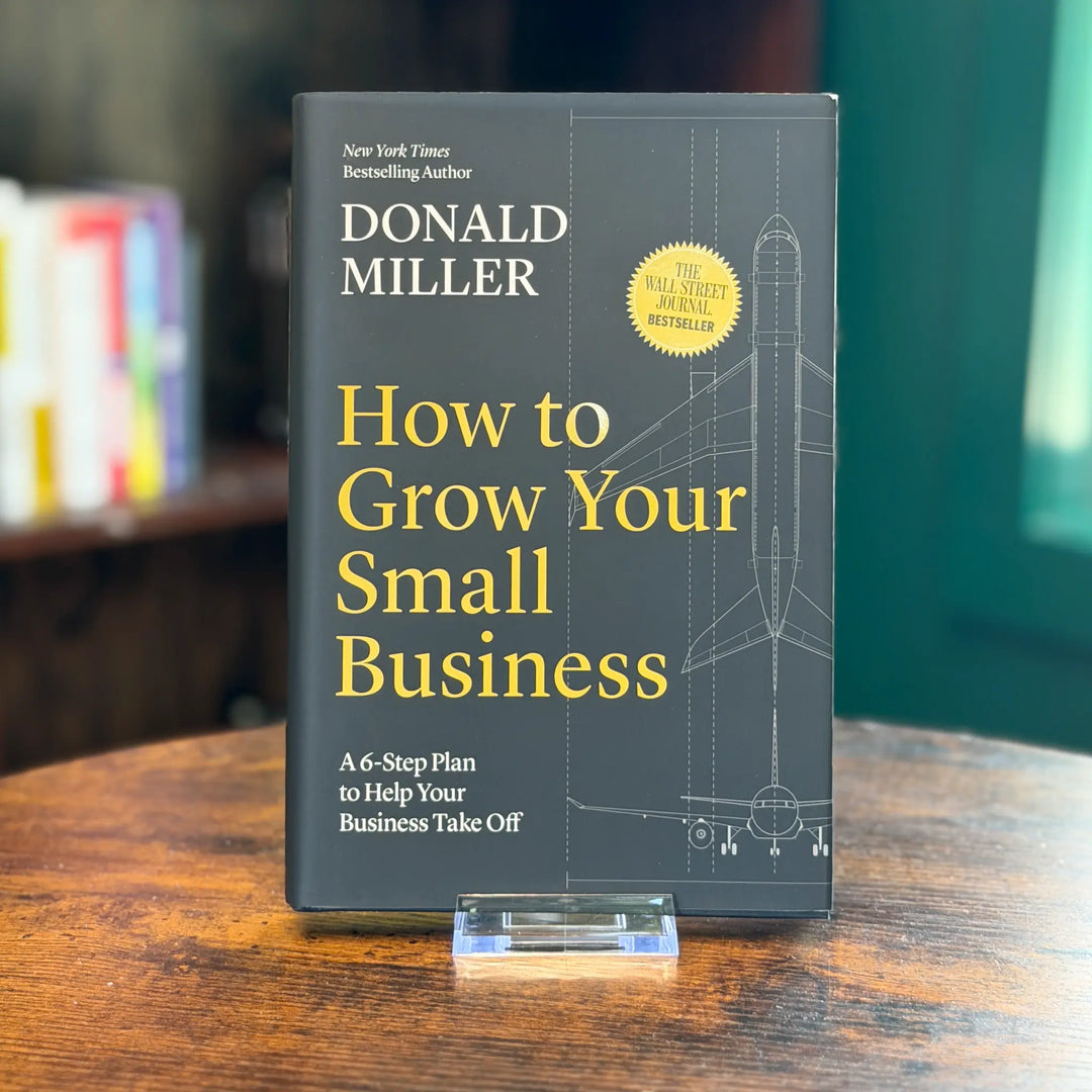 Book titled 'How to Grow Your Small Business' by Donald Miller on a wooden surface with a blurred bookshelf in the background.