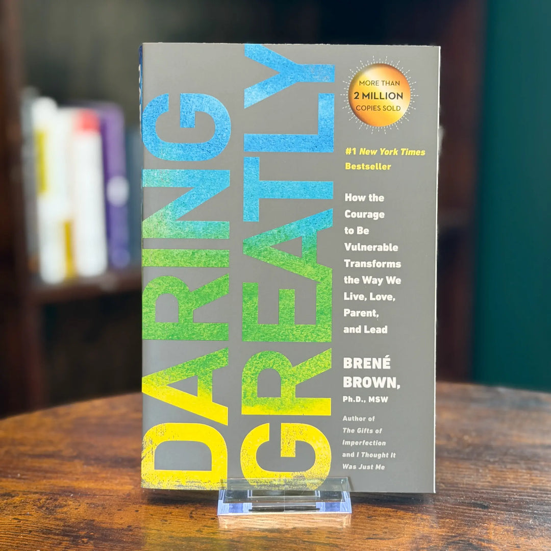 Book titled 'Daring Greatly' by Brené Brown on a wooden surface with a blurred bookshelf in the background.