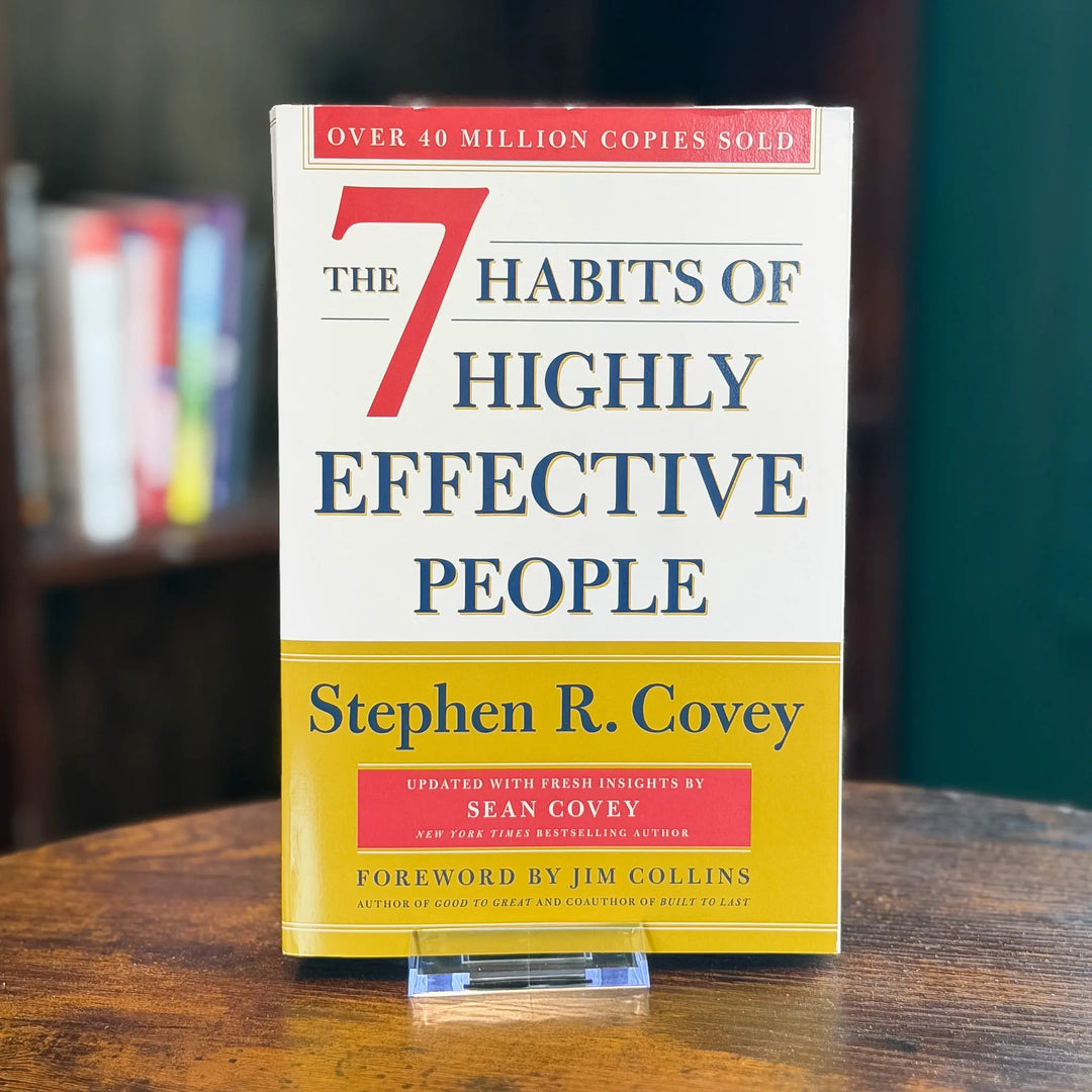Book titled 'The 7 Habits of Highly Effective People' by Stephen R. Covey on a wooden surface with a blurred bookshelf in the background.