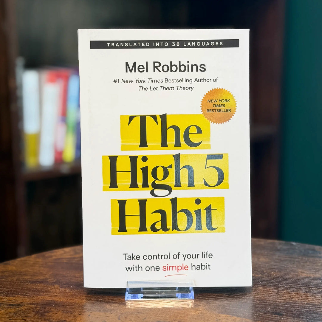 Book titled 'The High 5 Habit' by Mel Robbins on a wooden surface with a blurred bookshelf background.