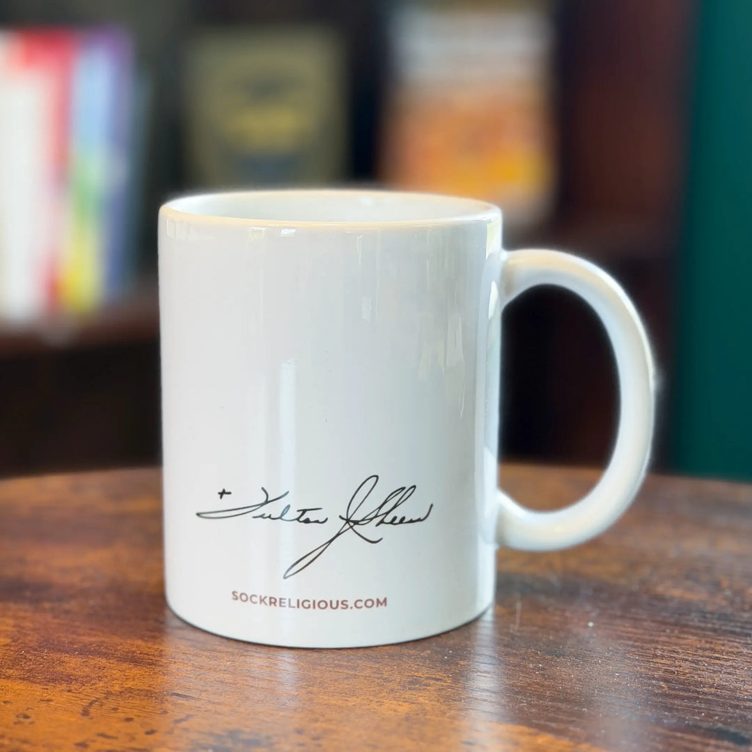White mug with a signature and website text on a wooden surface with blurred background