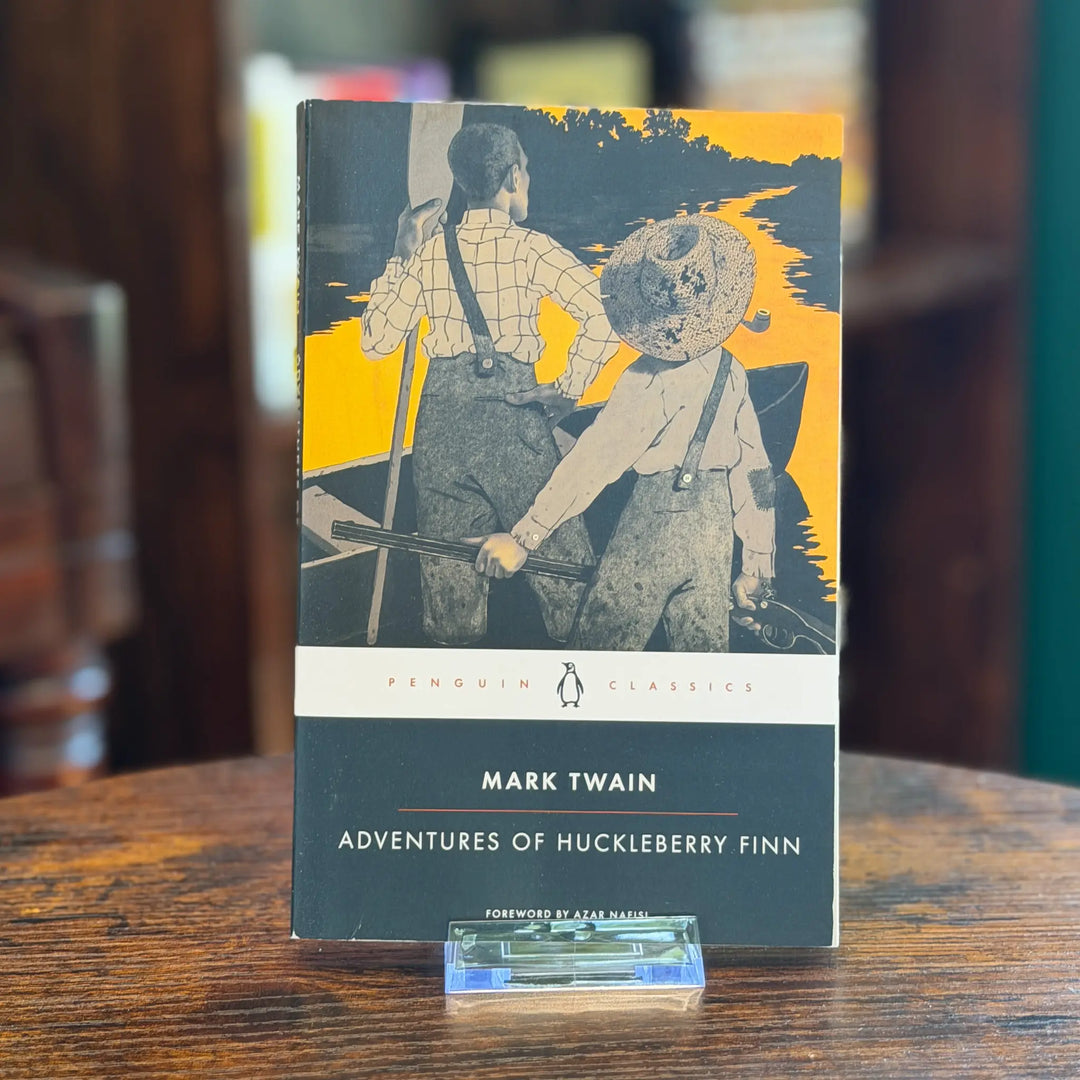 Book titled 'Adventures of Huckleberry Finn' by Mark Twain on a wooden surface.