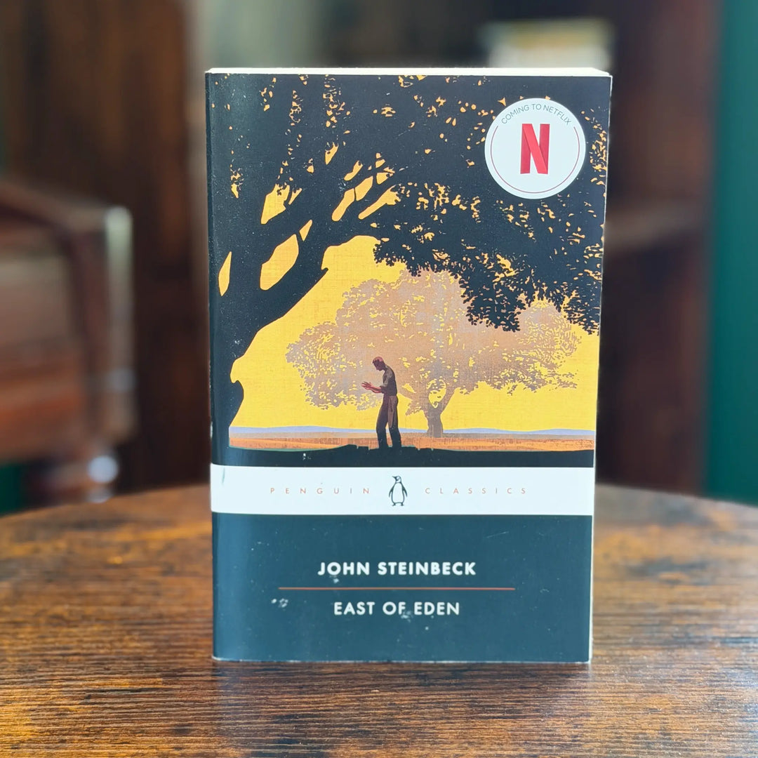 Book titled 'East of Eden' by John Steinbeck with a tree illustration on the cover, placed on a wooden surface.