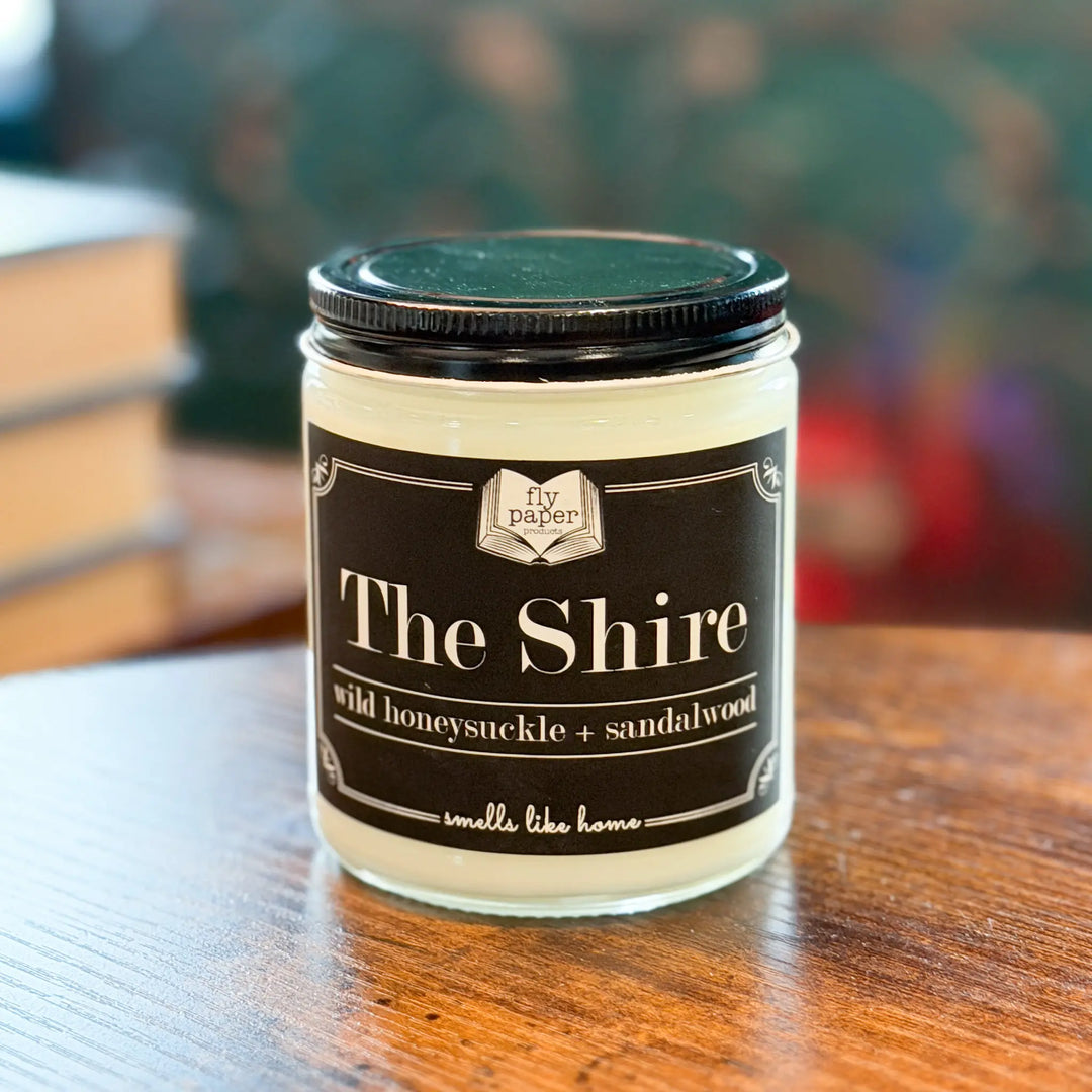 Jar of 'The Shire' candle with a black lid on a wooden surface, blurred background