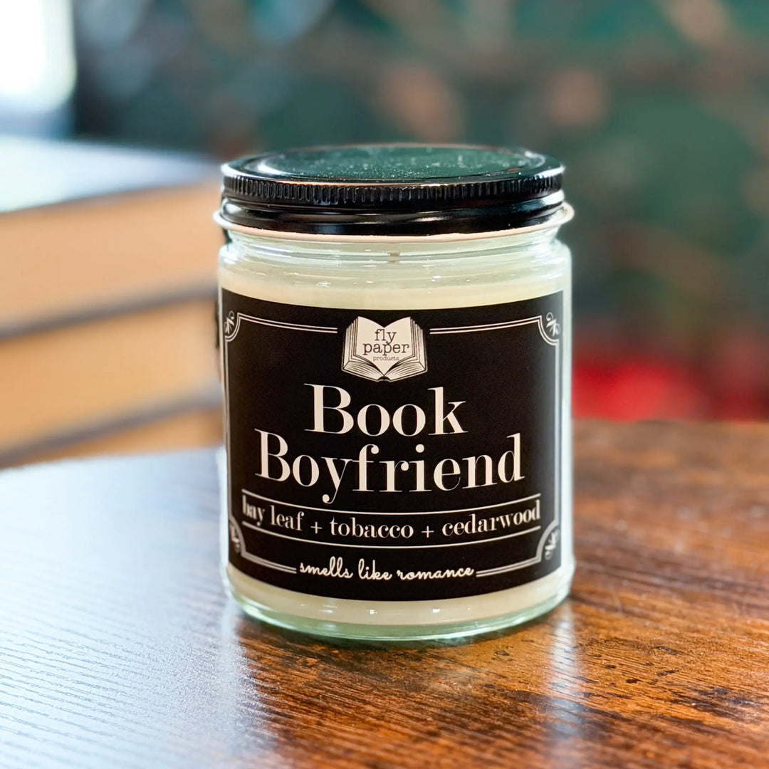 Candle jar labeled 'Book Boyfriend' on a wooden surface with a blurred background