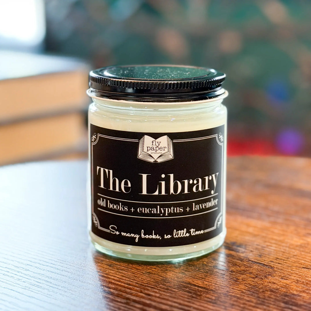 Candle jar labeled 'The Library' on a wooden surface with a blurred background