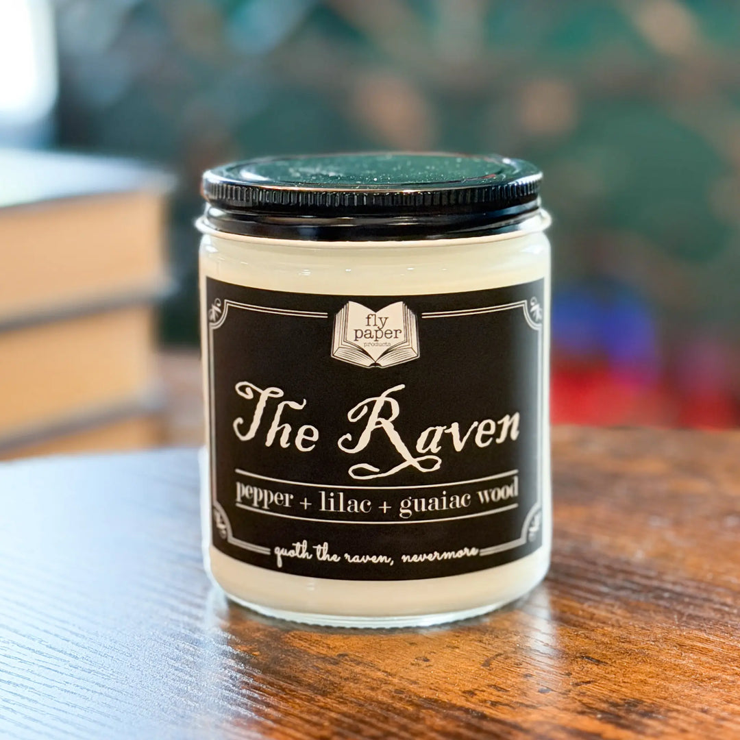 Candle jar labeled 'The Raven' with a black lid on a wooden surface.