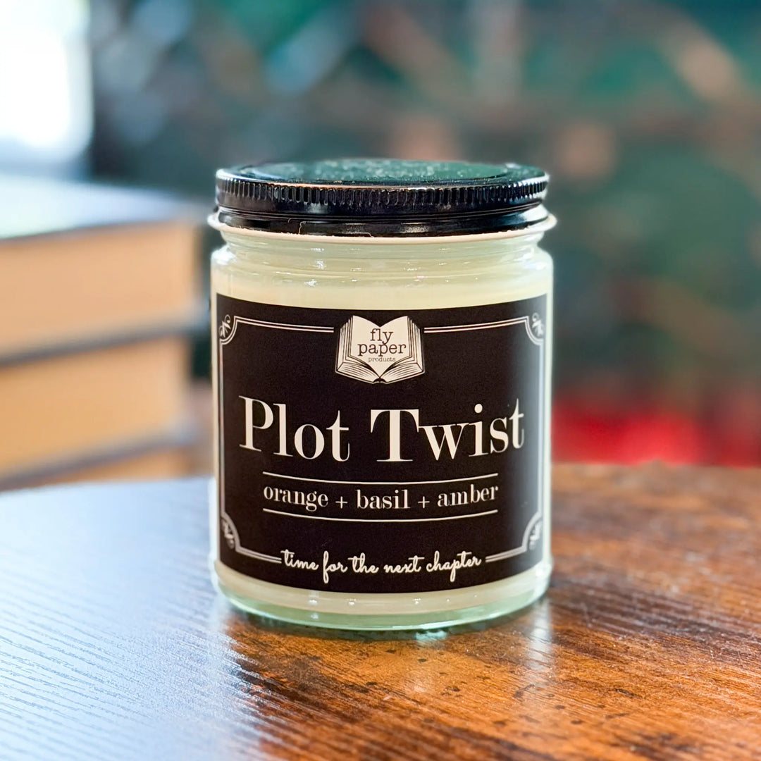 Candle jar labeled 'Plot Twist' with a black lid on a wooden surface.