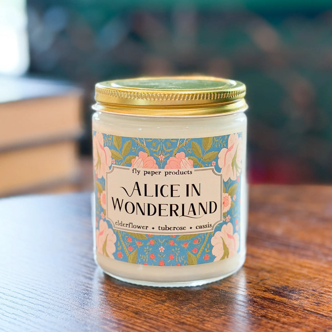 Candle jar labeled 'Alice in Wonderland' on a wooden surface with a blurred background