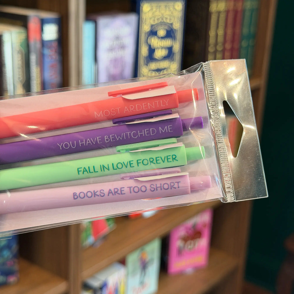 Set of colorful pens with humorous text in a clear packaging against a bookshelf background