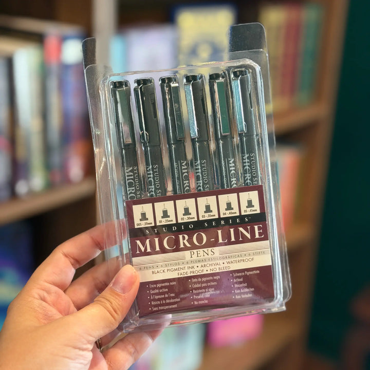 Pack of Studio Series Micro-Line pens held in front of a bookshelf.