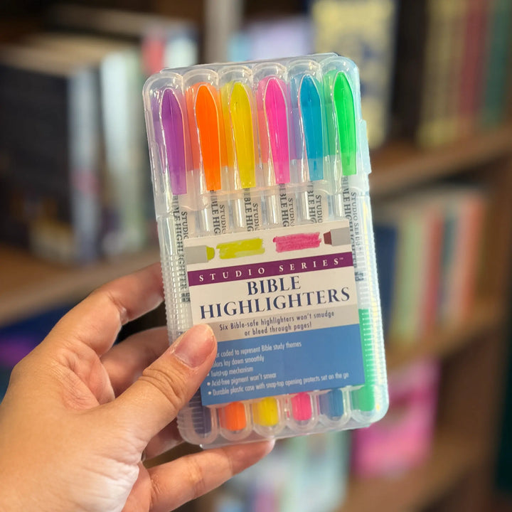 Pack of Bible highlighters held by a hand with a blurred bookshelf background