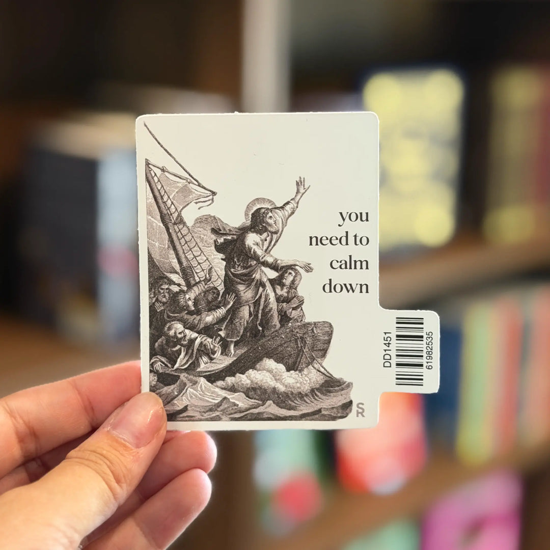 Sticker with a black and white illustration of a person calming a stormy sea, held by a hand with a blurred bookshelf background.