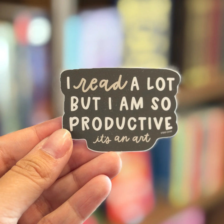 Hand holding a sticker with text in front of a blurred bookshelf background