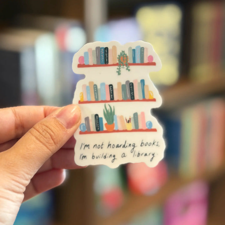 Sticker of a bookshelf with books and plants held by a hand in front of a blurred bookshelf background.