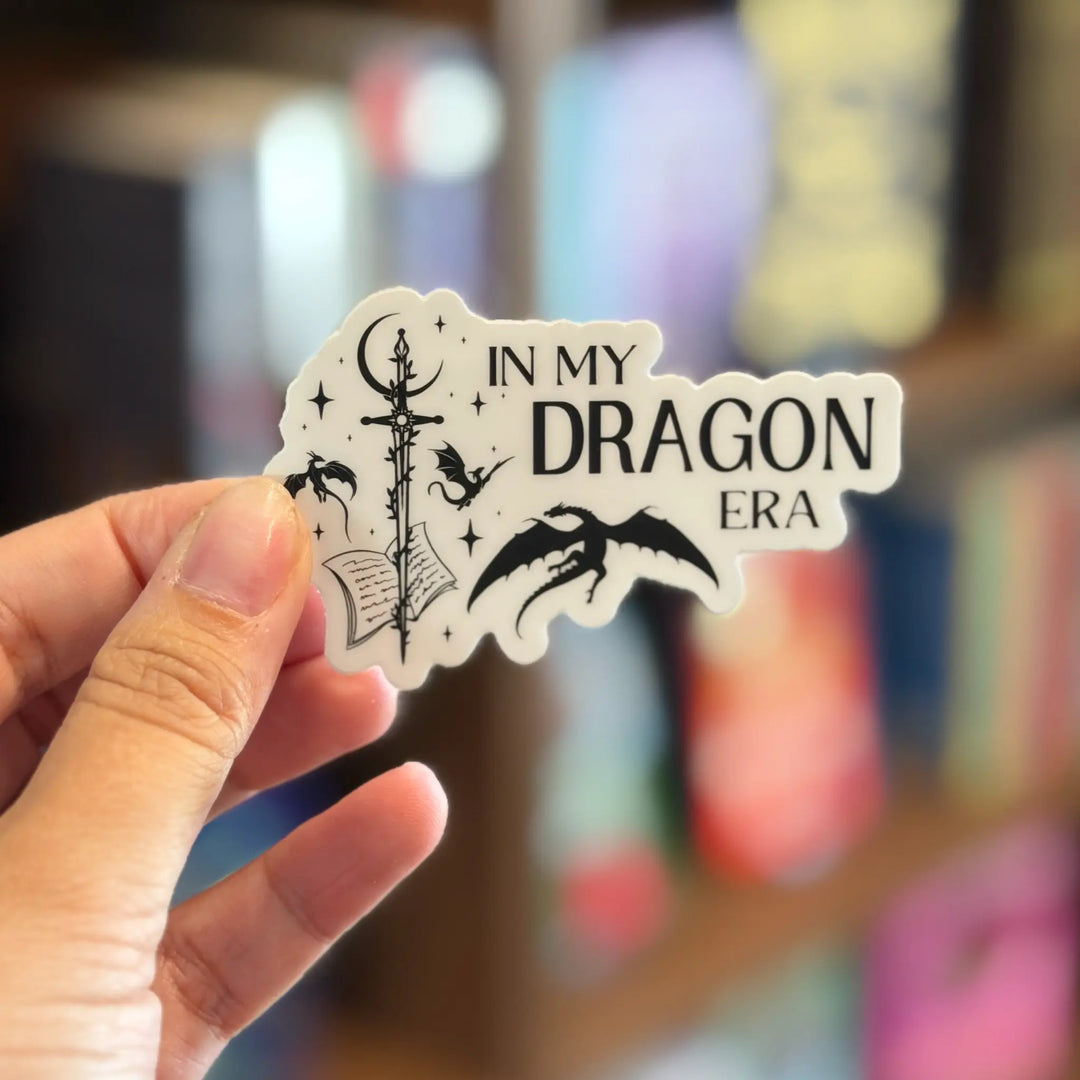 Hand holding a 'In My Dragon Era' sticker with a blurred background