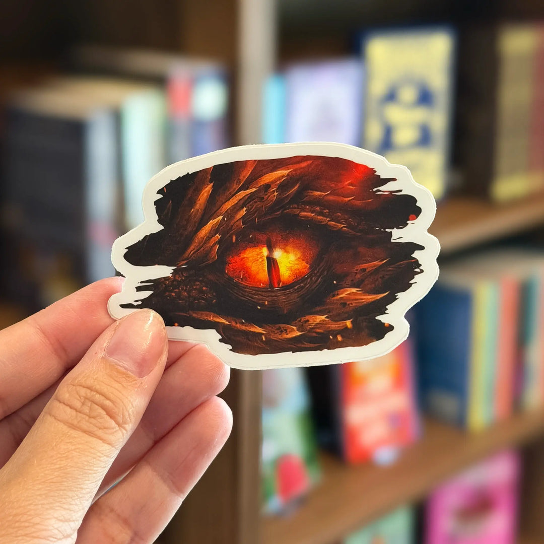 Hand holding a dragon eye sticker in front of a bookshelf