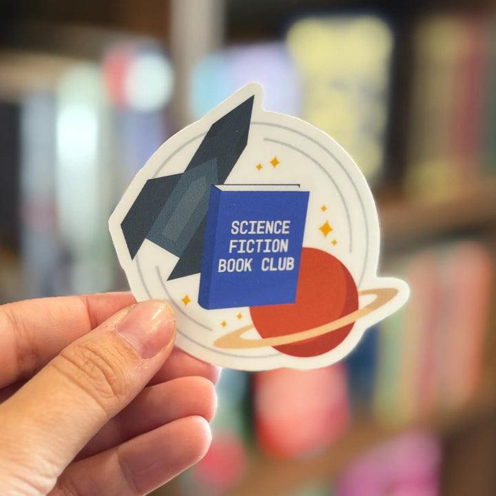 Sticker for Science Fiction Book Club held by a hand with a blurred bookshelf background