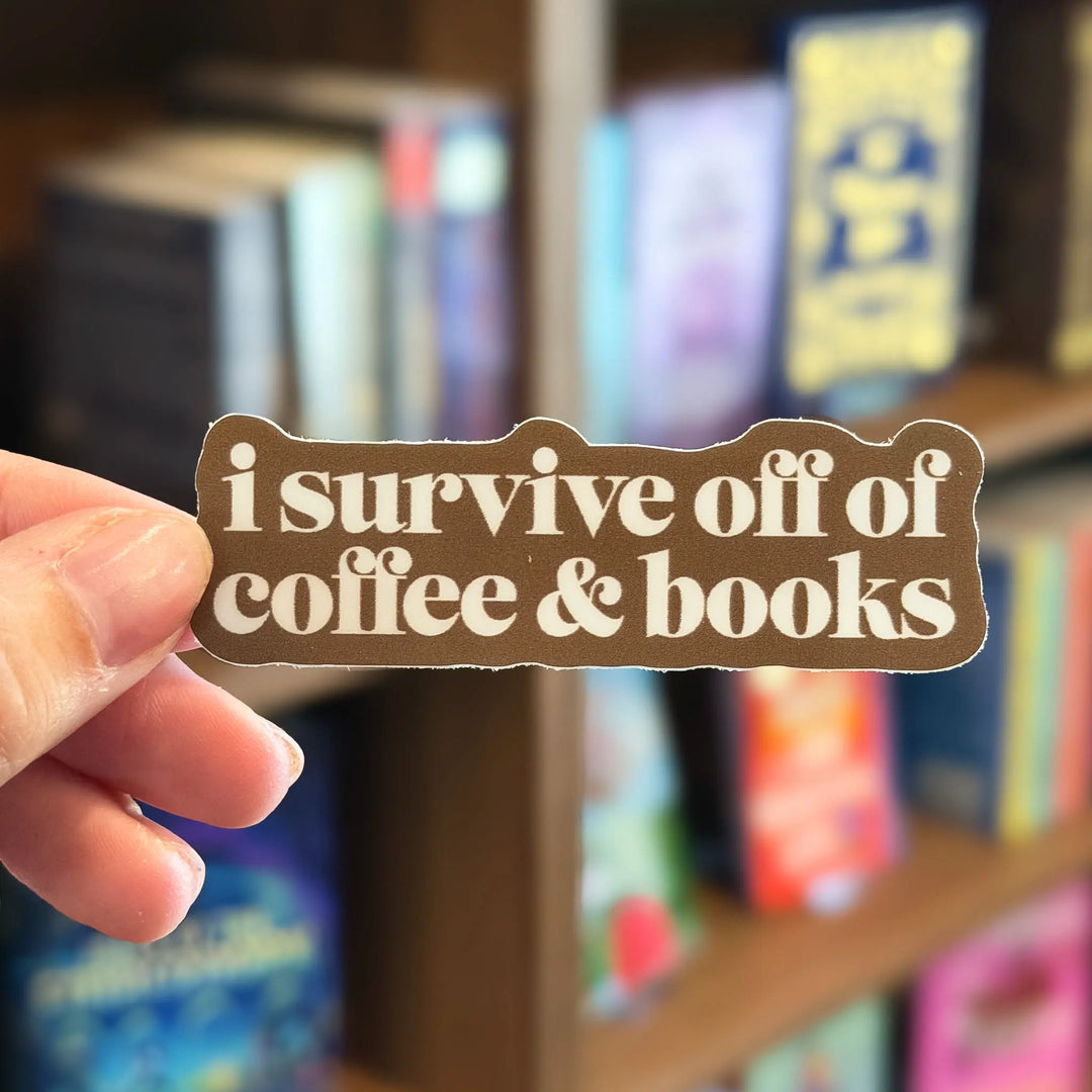 Hand holding a sign with 'i survive off of coffee & books' in front of a bookshelf.
