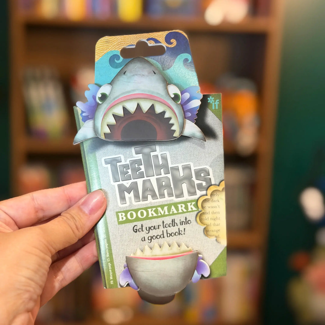Shark-themed bookmark packaging held by a hand with a blurred bookshelf background
