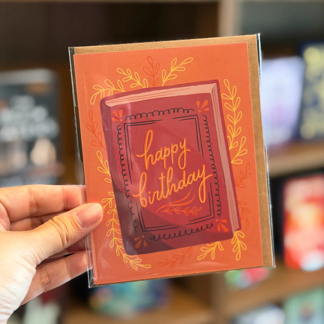 Hand holding a birthday card with decorative text and border. Text reads 'happy birthday'