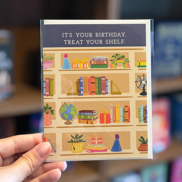 Card with a birthday message and illustration of a bookshelf held by a hand. Text reads &