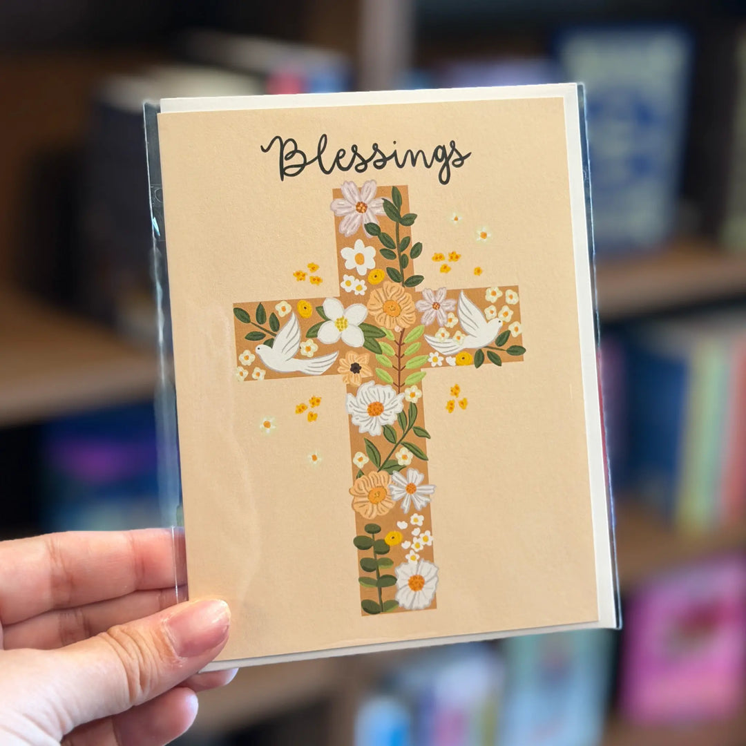 Card with a cross design and 'Blessings' text held by a hand against a blurred background