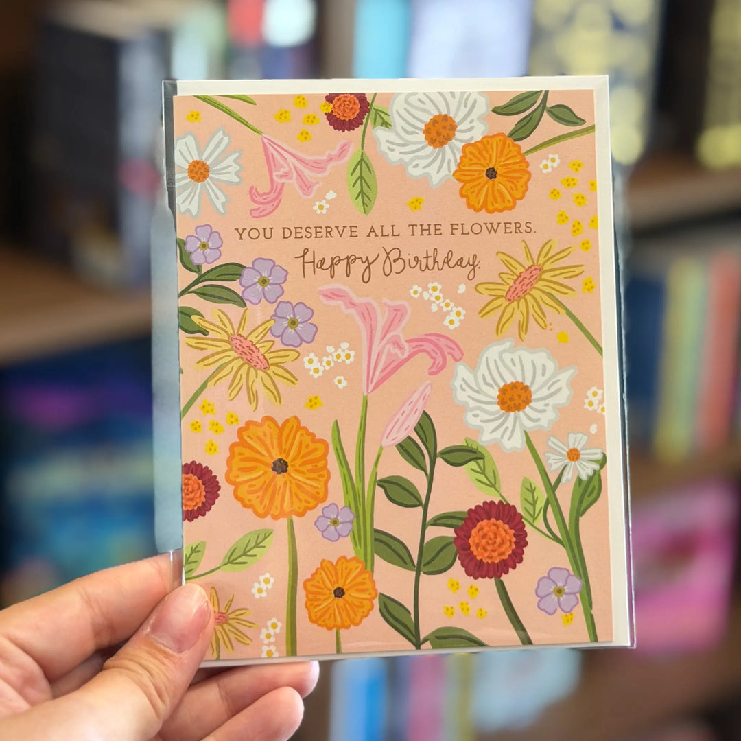 Hand holding a birthday card with floral design and text. Text reads 'You deserve all the flowers. Happy birthday'