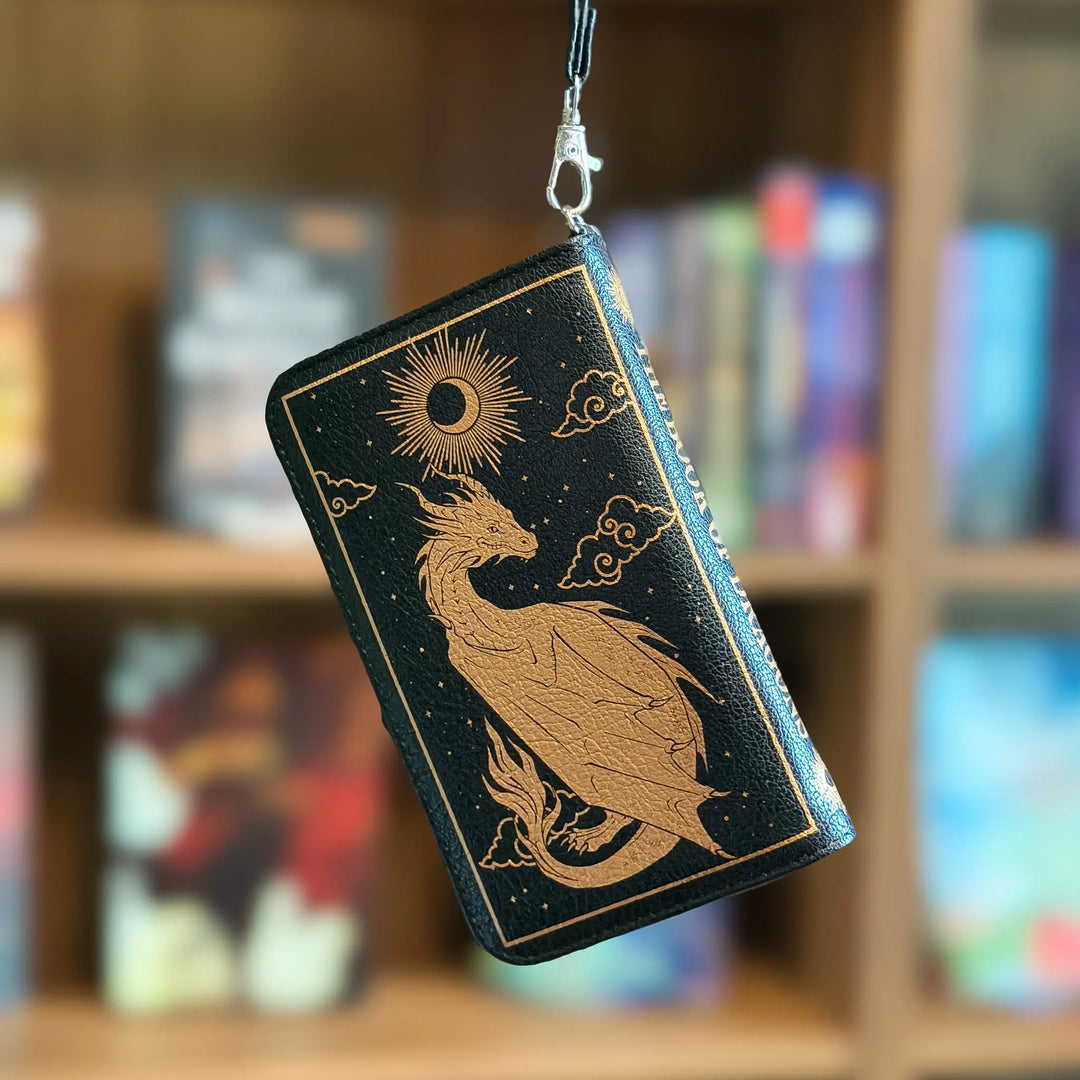 Black phone case with gold dragon design hanging on a hook against a blurred bookshelf background