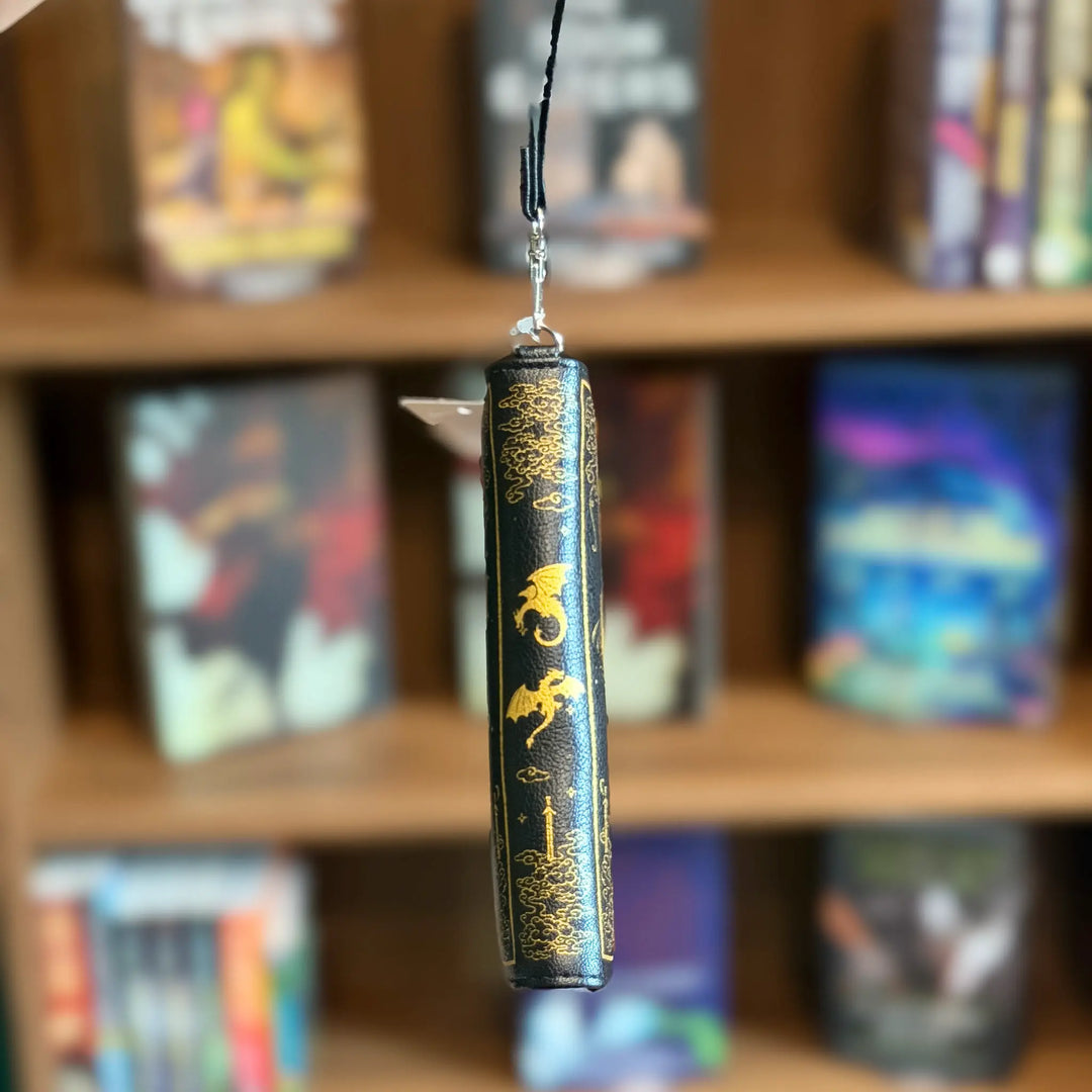 Black wallet with gold text and designs hanging against a bookshelf background
