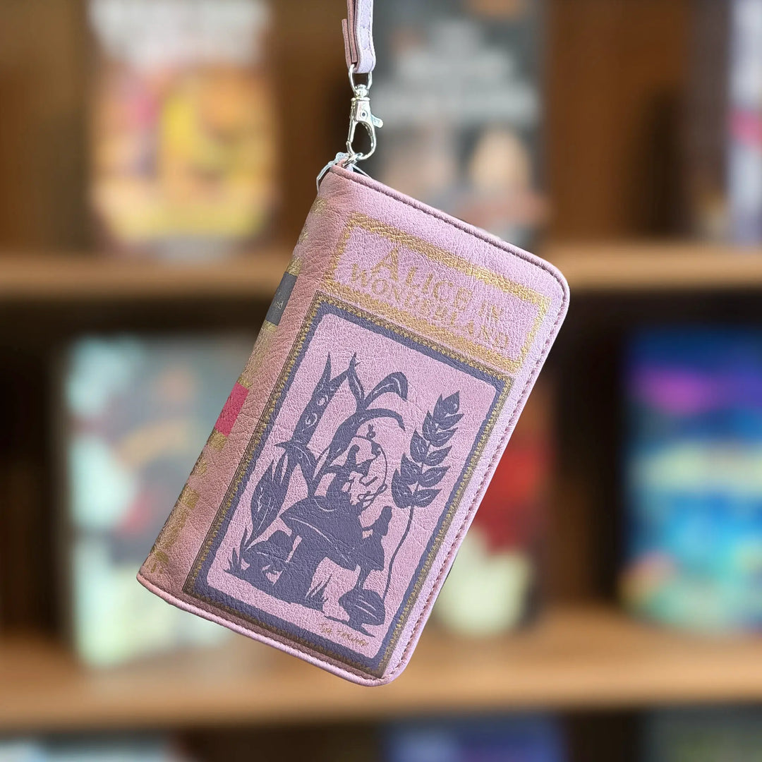 Pink book-shaped wallet with a design on a blurred bookshelf background