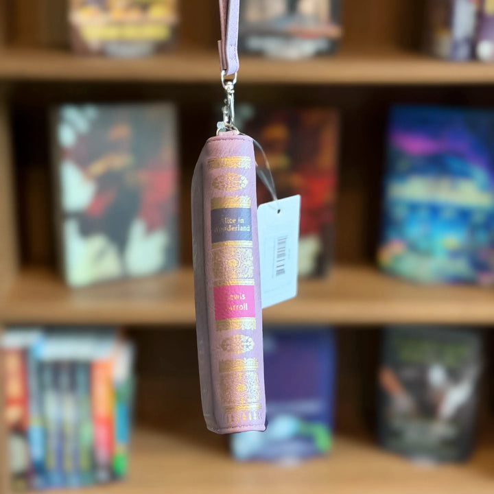 Purple book-shaped wallet with a tag against a blurred bookshelf background