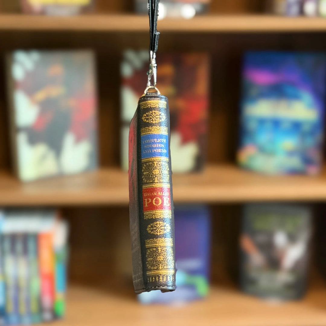Decorative wallet shaped like a book with gold text on a blurred bookshelf background